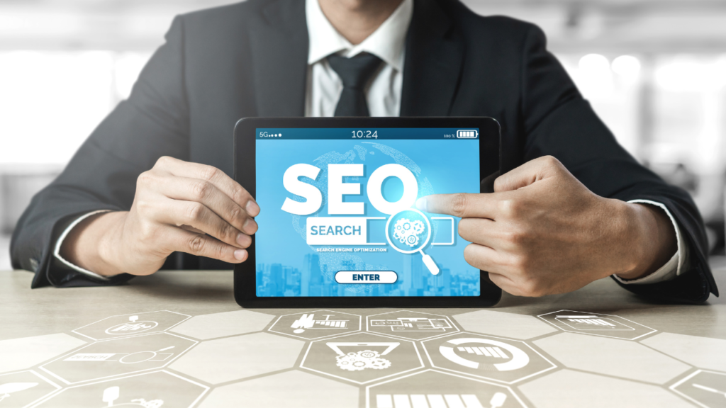 A business professional in a suit holding a tablet displaying SEO Services with digital marketing icons in the background.
